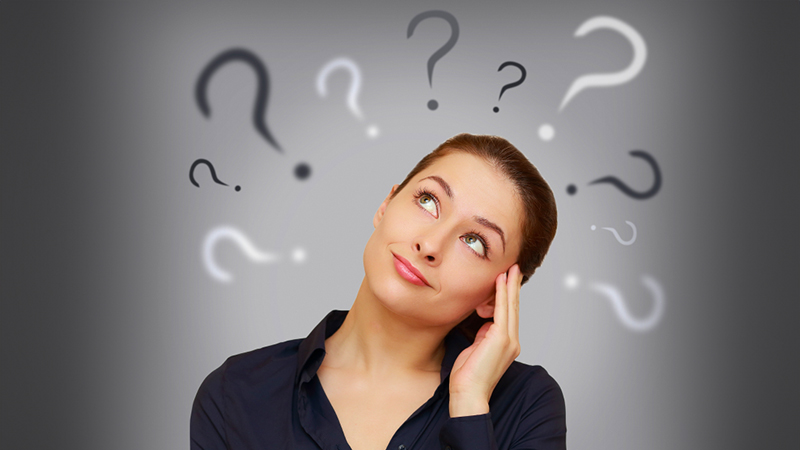 Female student loan borrower looking up at question marks above her head on grey background.